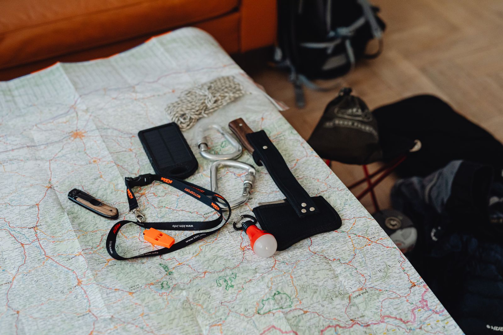 Line-art of a packed backpack standing open by a front door, its contents laid out beside it in labeled groups — water, food, shelter, fire, first aid, and tools.