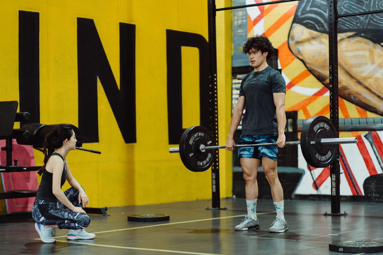 A split-panel comparison: on the left, a man performing a barbell bench press with a controlled lowering phase, elbows tracking slightly outward, chest up; on the right, the same man performing a dumbbell row with one knee on a bench, hip engaged and core braced, pulling the weight with retracted scapula and neutral spine.