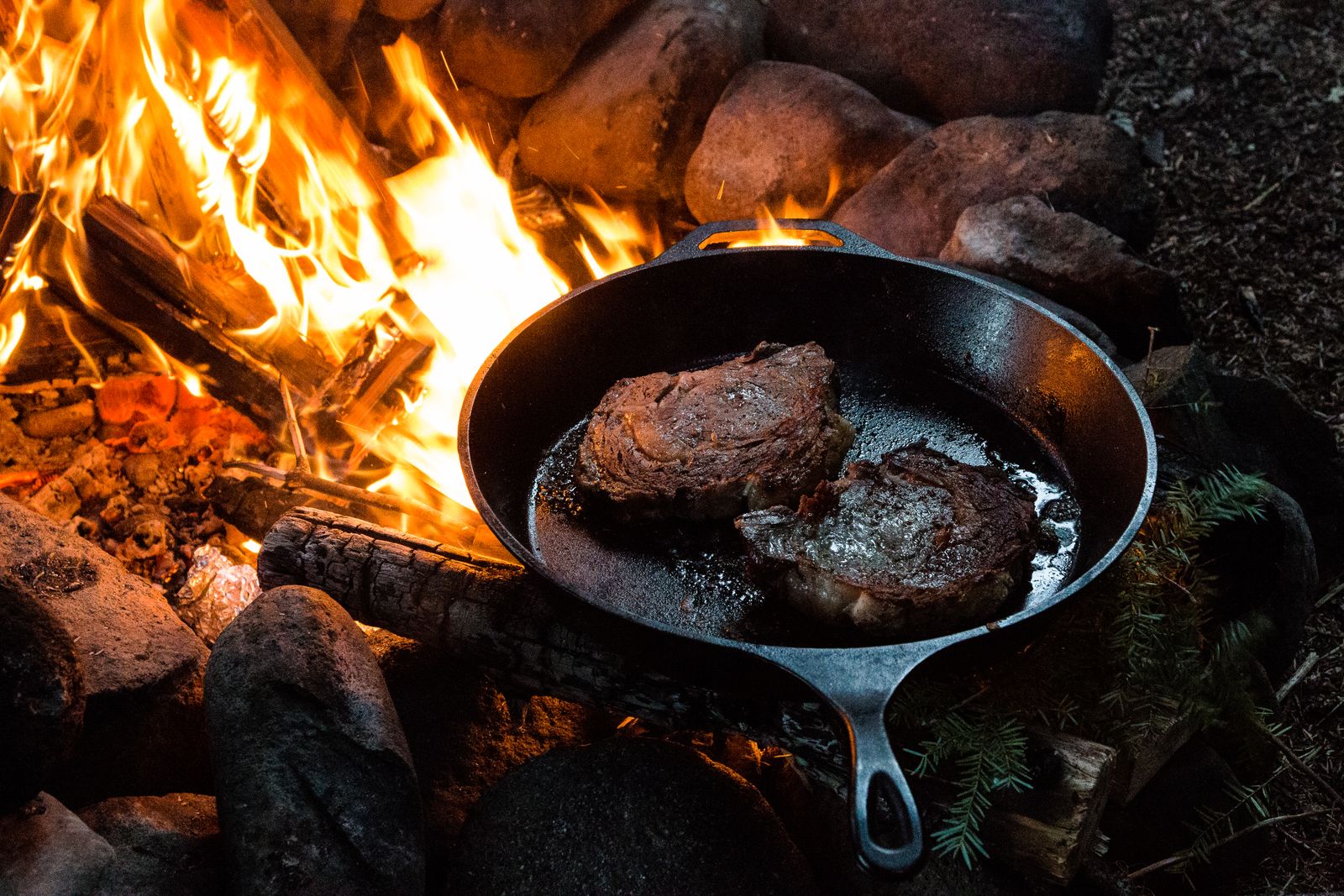 A side-by-side comparison of two steak-cooking methods: pan-sear showing a steak browning in a cast-iron skillet with butter, garlic, and herbs, and reverse-sear showing a steak in a low oven followed by quick searing in a smoking hot skillet.