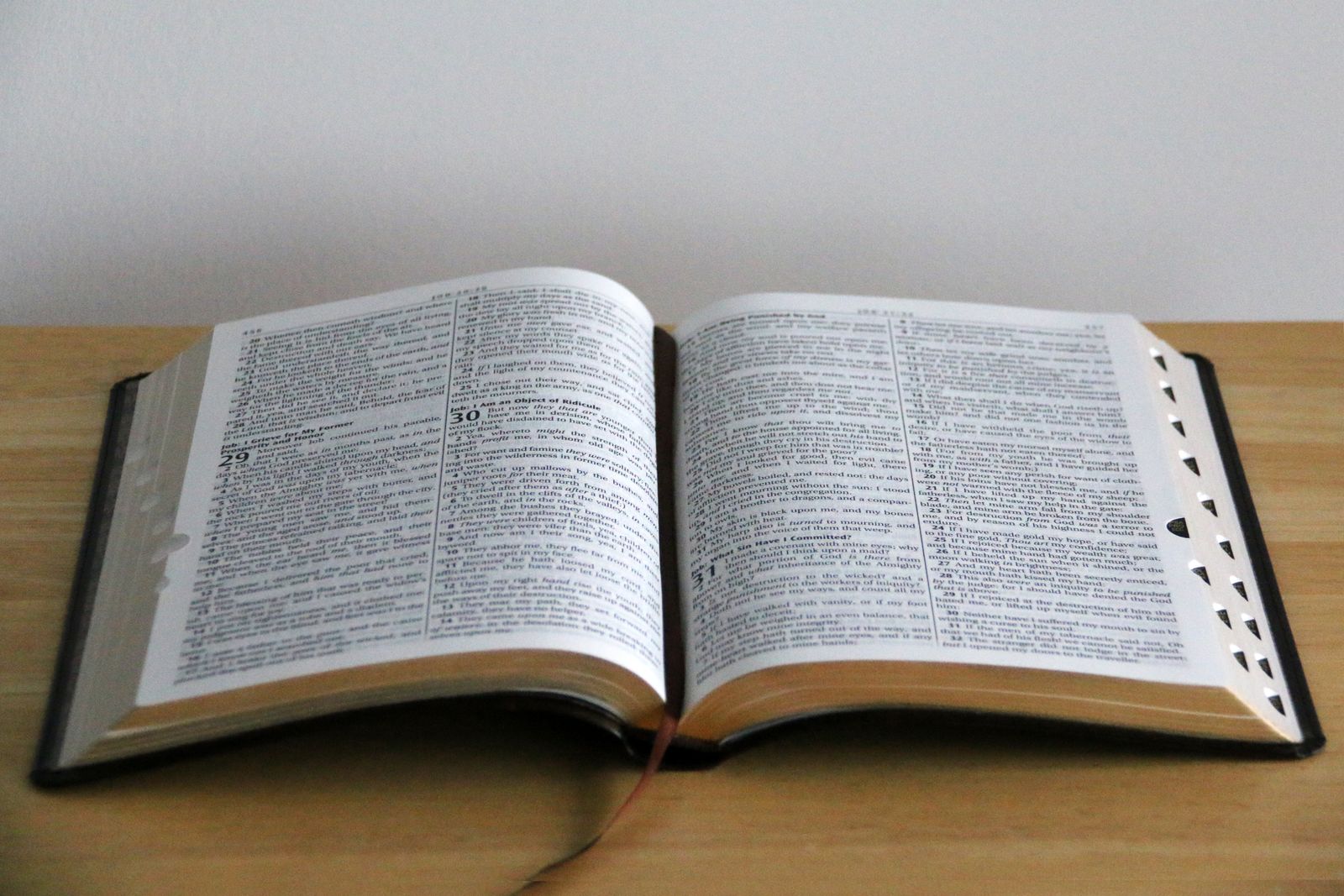 An open Bible on a wooden table beside a coffee mug, a pen, and a notebook, lit by morning light through a window.