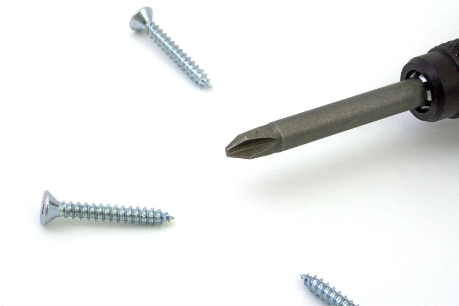 A hand pressing a screwdriver through a rubber band laid over a stripped screw head, with locking pliers and a screw-extractor set arranged nearby on a wooden workbench.