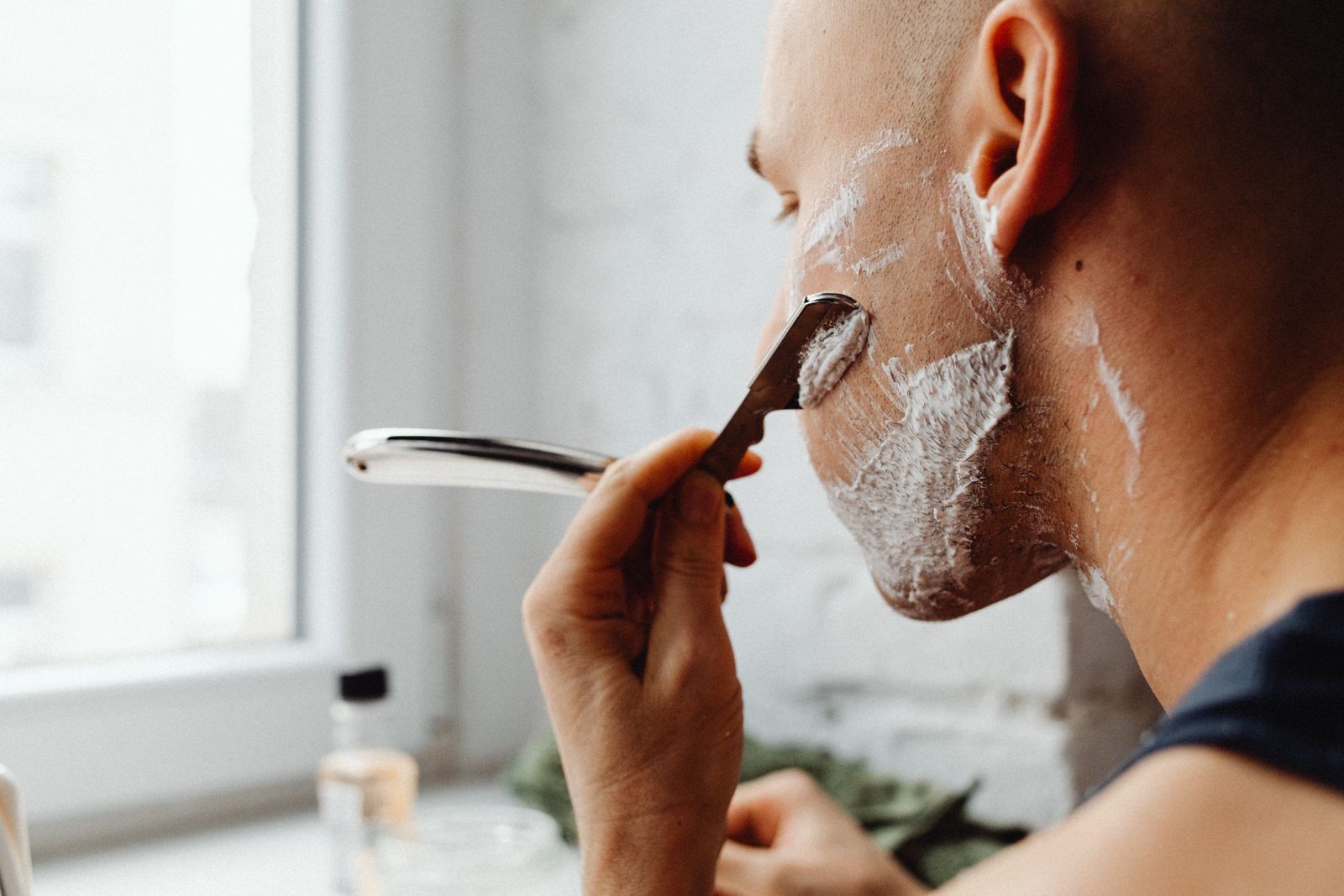 A side-view diagram showing a safety razor held at the correct 30-degree angle to the skin, with labeled zones of the face (cheeks, chin, neck, jawline) indicating different grain directions as arrows, and a timeline showing three shaving passes from left to right: with-the-grain, across-the-grain, and against-the-grain.