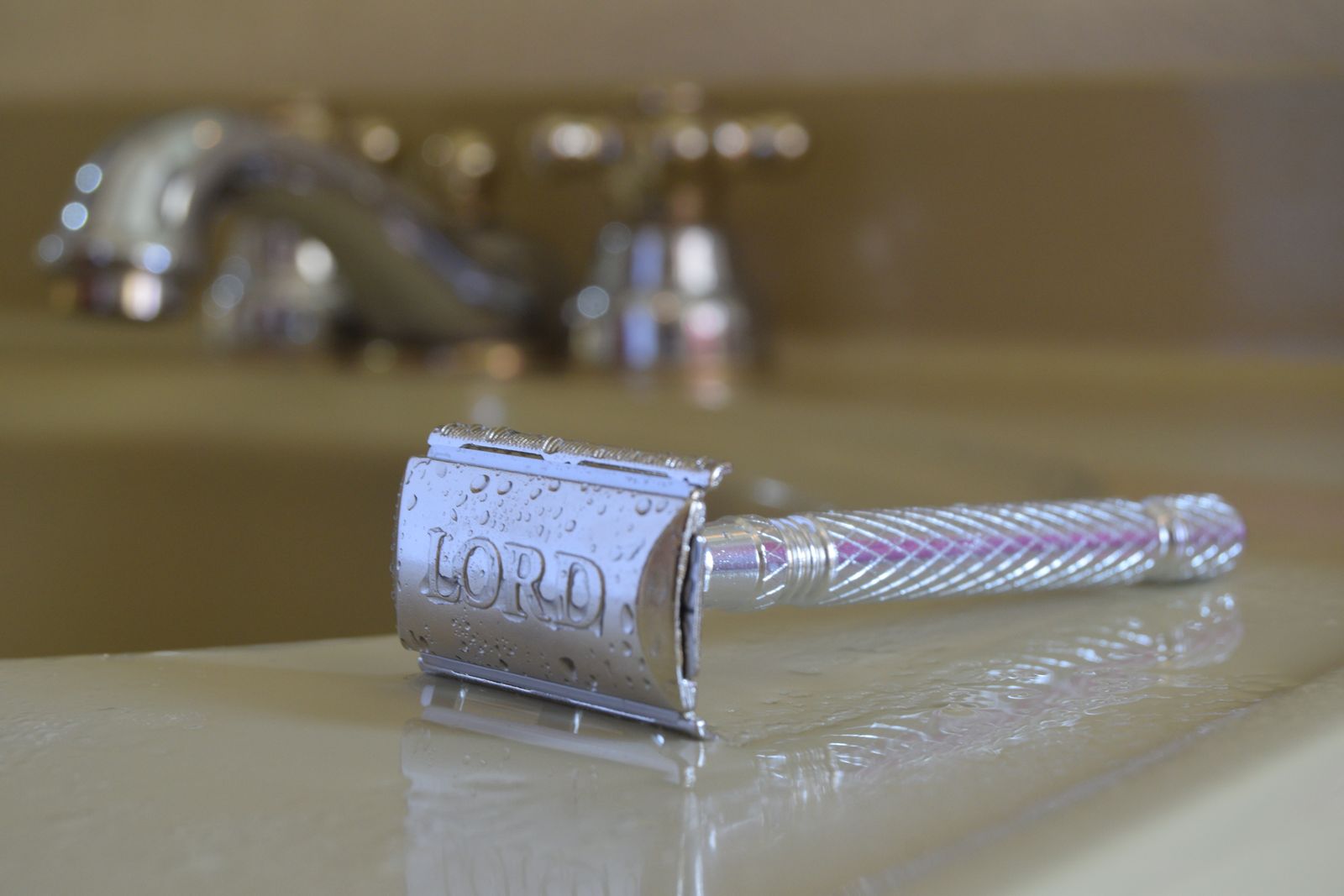 A close-up cross-section diagram showing a safety razor head with blade loaded at the correct 30-degree angle to skin, with labeled elements: handle orientation, blade edge, skin surface, and short stroke direction indicated by a curved arrow. Secondary inset shows hand position gripping the razor with light tension.